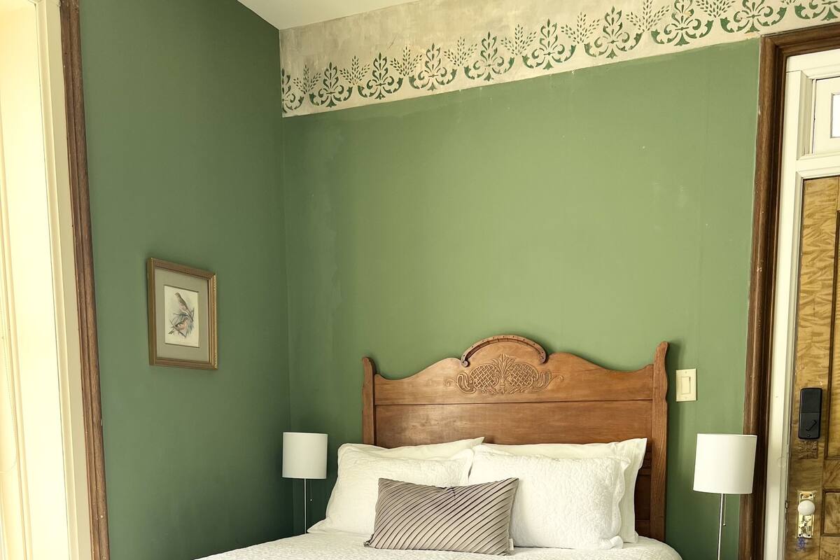 Una cama bien hecha con cabecera de madera, dos lámparas de noche y un cuadro enmarcado en la pared.