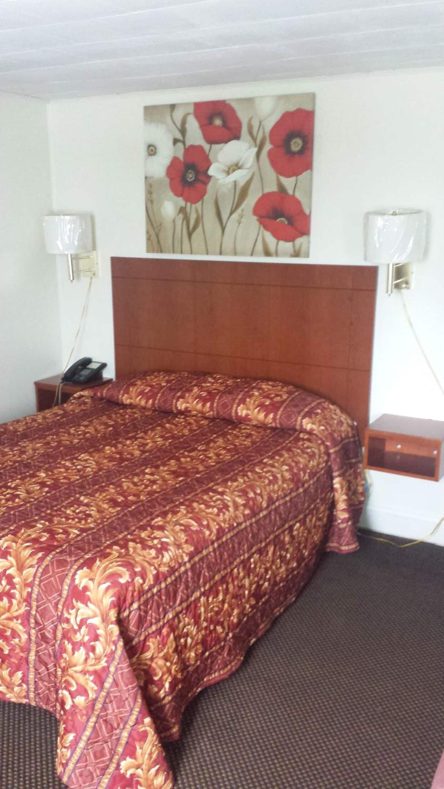 Quarto de hotel com uma cama grande, cabeceira de madeira, pintura de flores na parede e luminárias laterais.