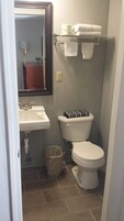 A small bathroom with a sink, toilet, and a mirror. There is a towel rack above the toilet and a trash can next to it.
