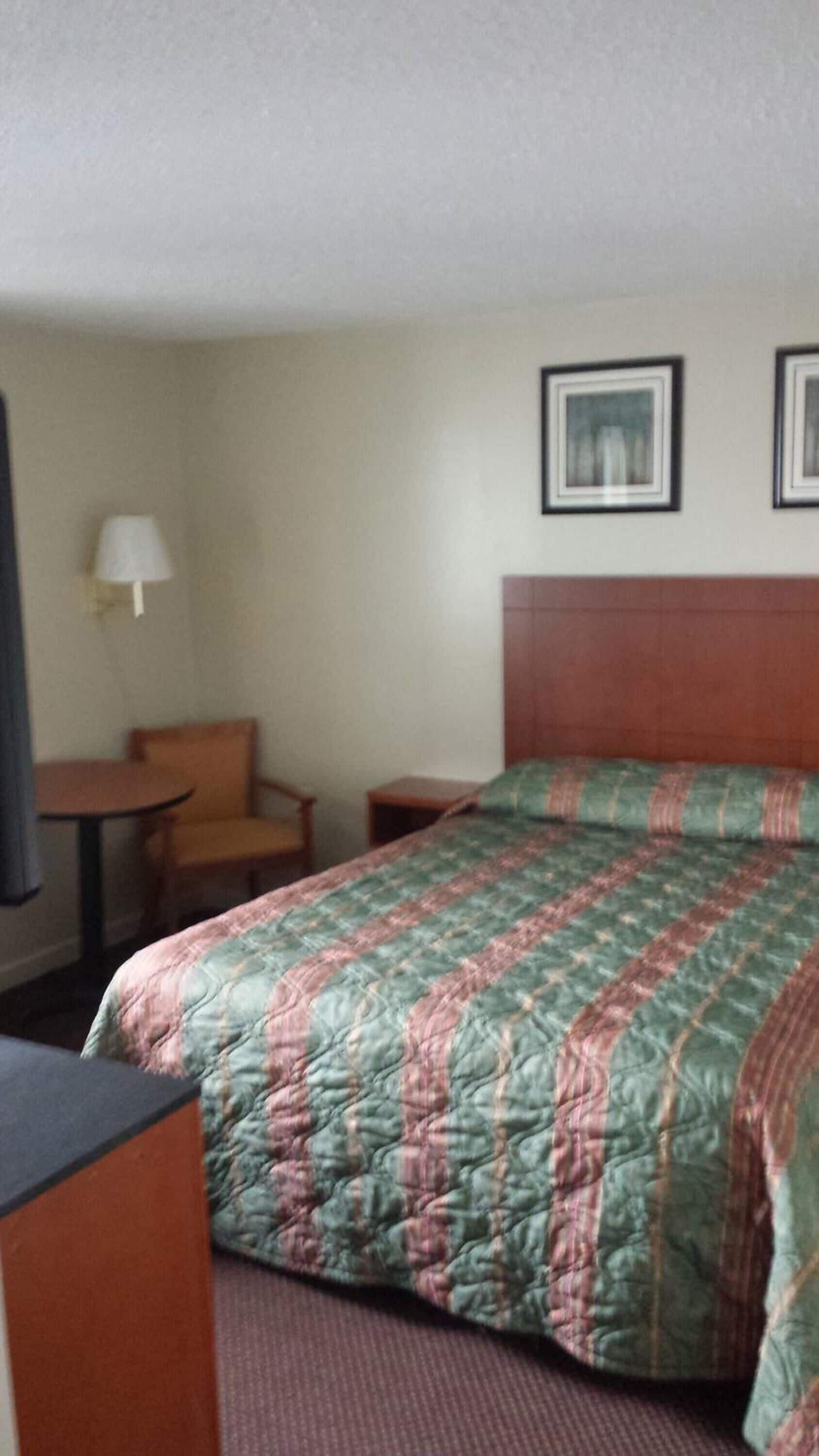 A hotel room with a bed, a small table, a chair, and a lamp.