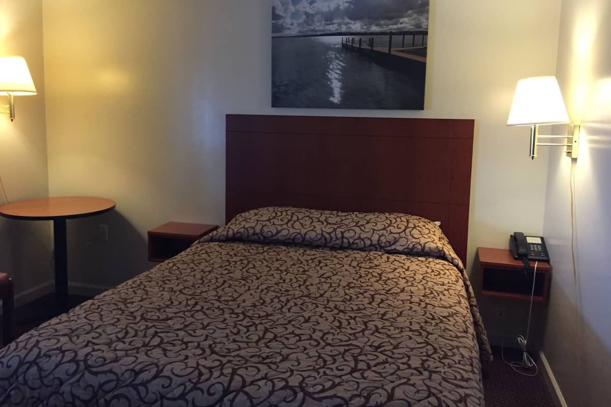 A hotel room with a bed, two bedside tables, a round table, a painting of a cloudy sky over water, and two wall-mounted lamps.