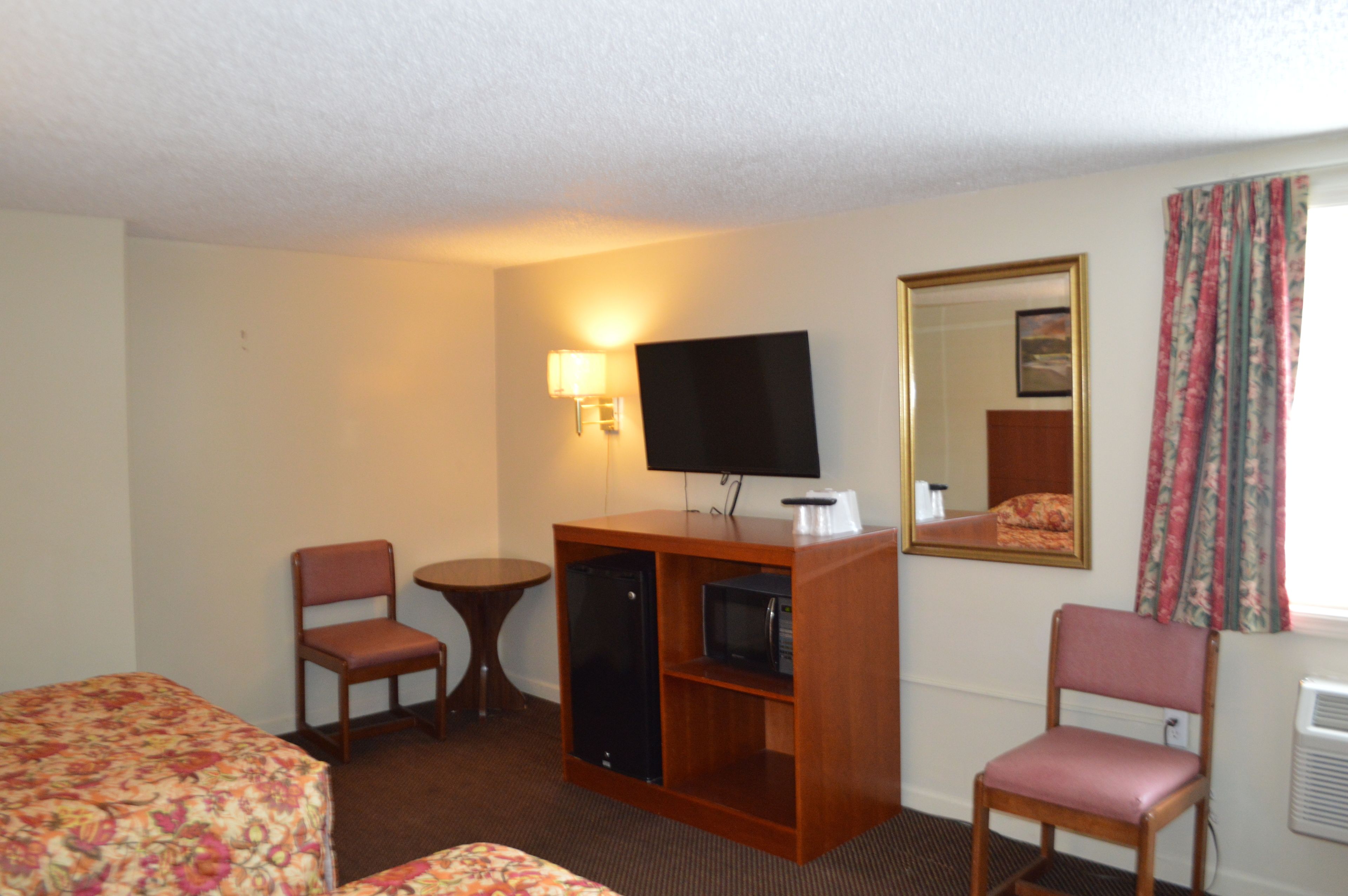 Une chambre d’hôtel comprenant un lit, un bureau avec une télévision, une chaise, une petite table et un miroir.