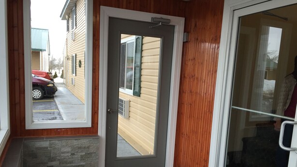 A wooden exterior door with a glass panel, a stone step, and a metal doormat. - Royal Inn Motel (Watertown)