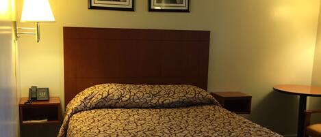 Una habitación de hotel con una cama, una mesita de noche con lámpara y dos cuadros en la pared.