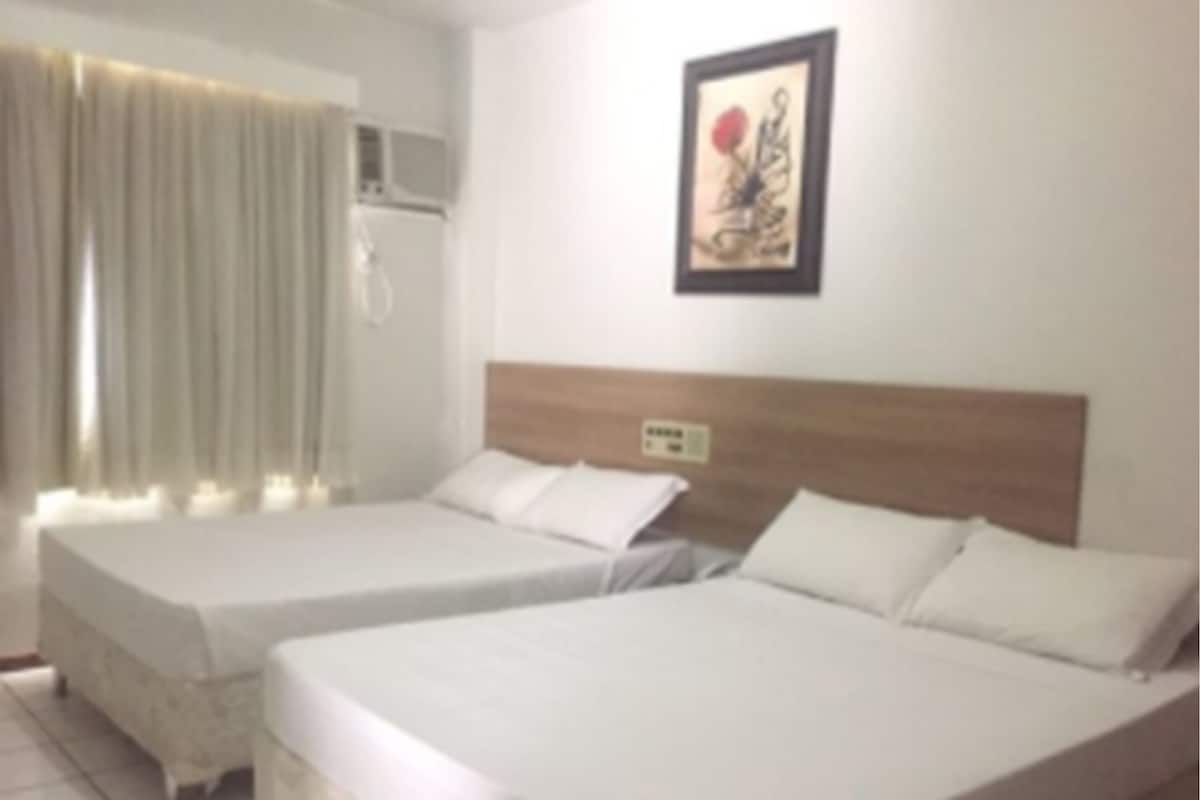 A hotel room with two single beds, a wooden headboard, a framed artwork on the wall, and a window with curtains.