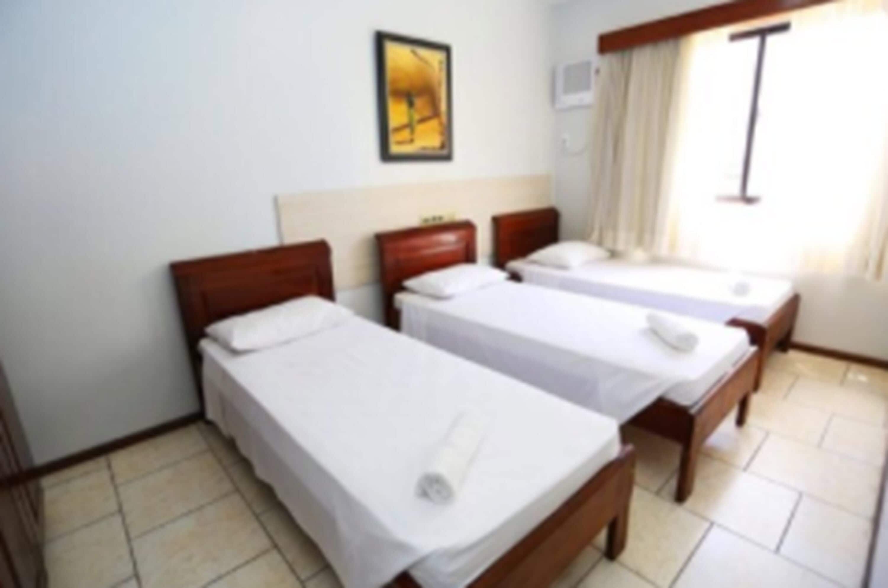 A hotel room with two single beds, a wooden headboard, a small table, and a window with curtains.