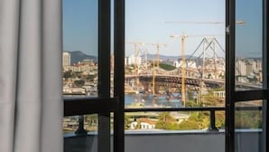 Une chambre d’hôtel dotée d’une grande fenêtre donnant sur un chantier de construction avec des grues et un pont.