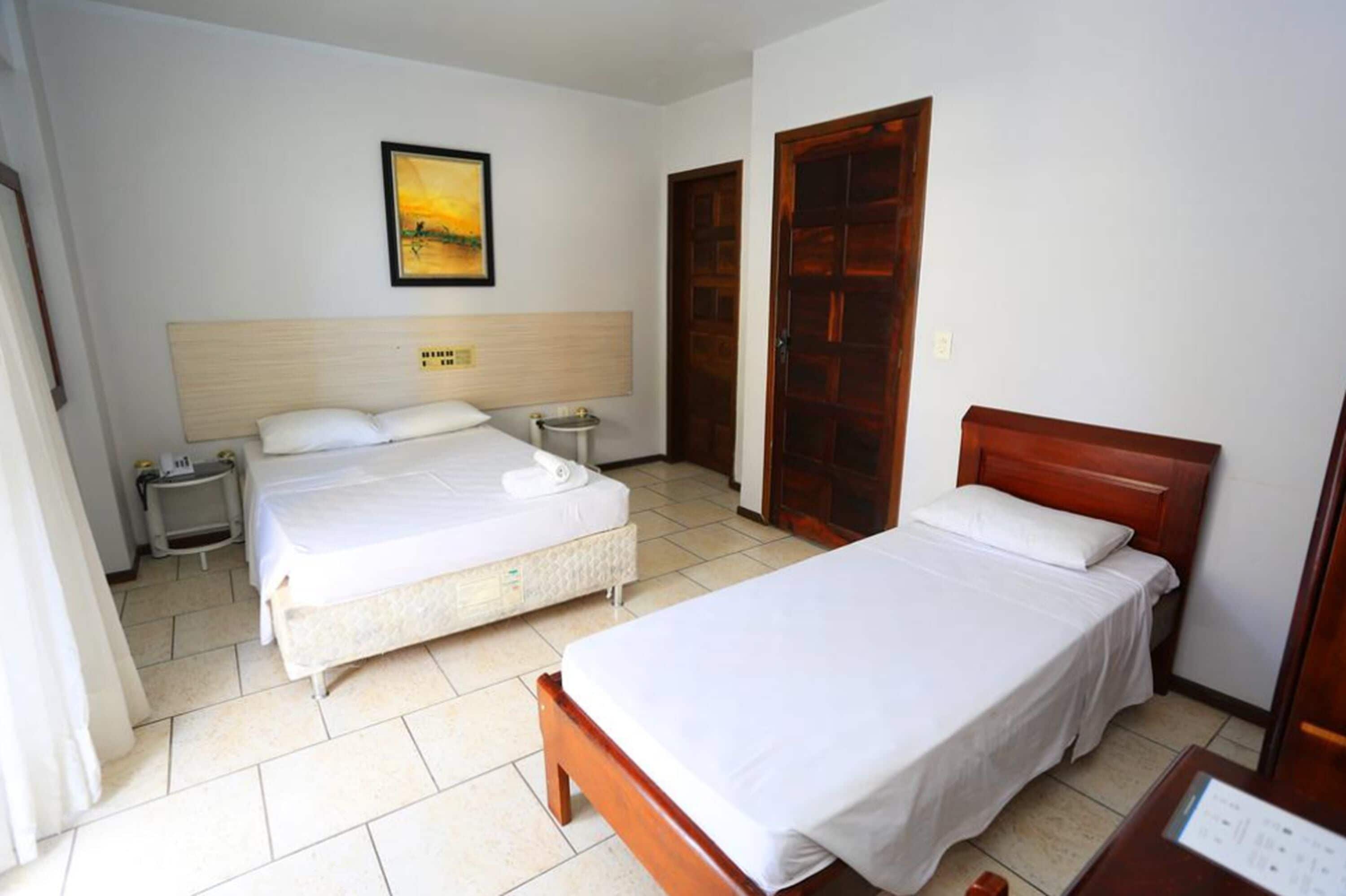 A hotel room with two beds, a wooden headboard, a nightstand, a bedside table, a framed picture on the wall, and a wooden door.