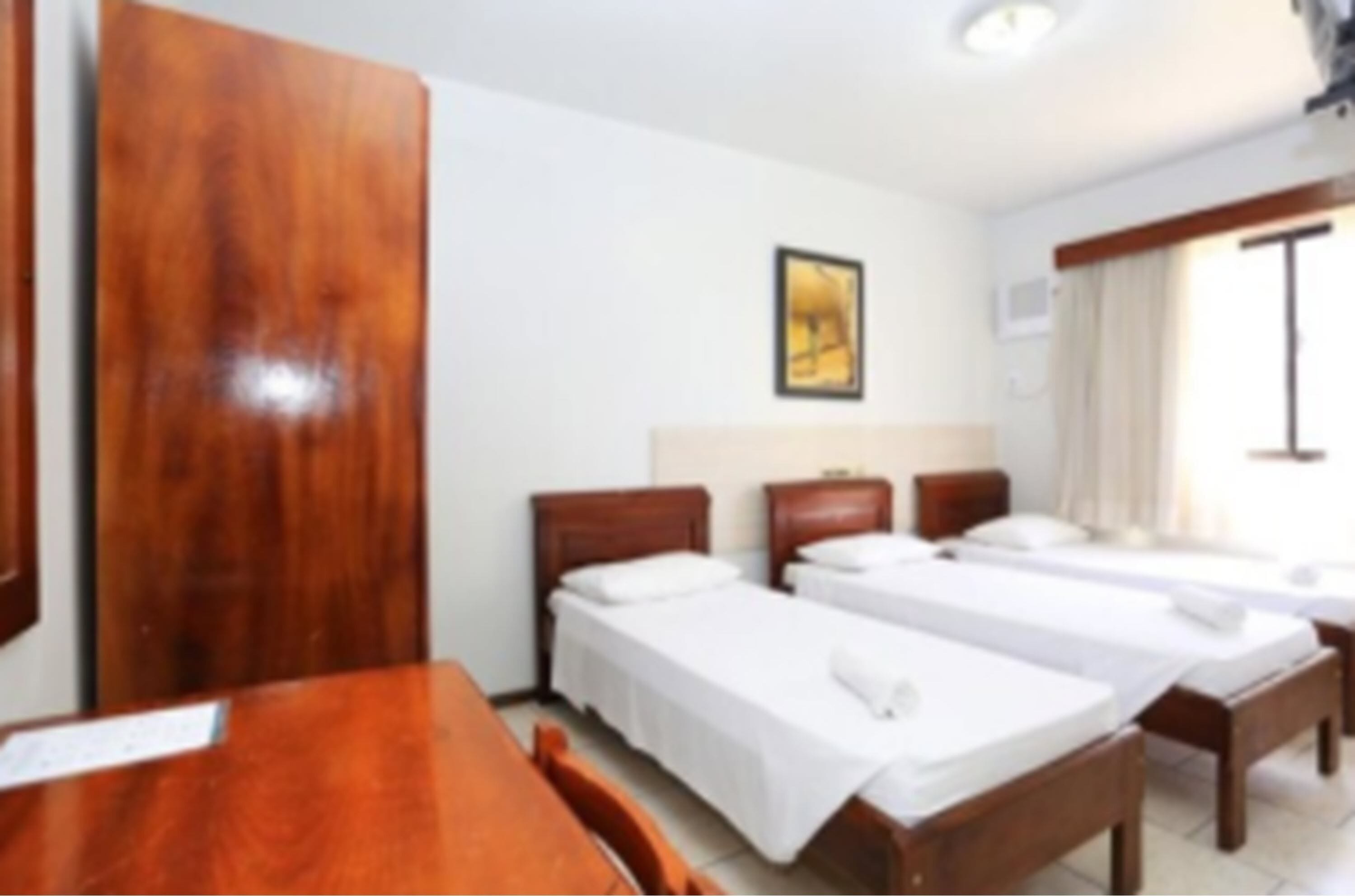 A hotel room with two single beds, a wooden table, and a framed picture on the wall.