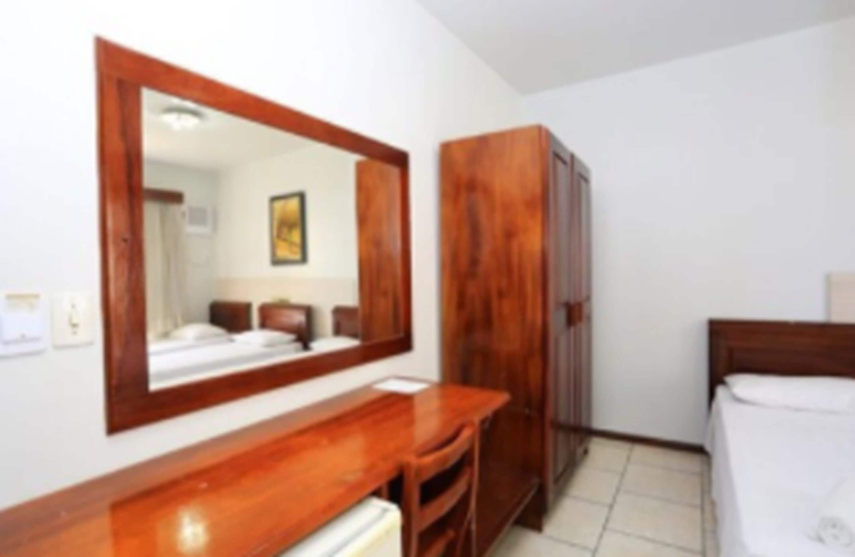 A hotel room with a wooden dresser, a large mirror, a bed, and a wardrobe.