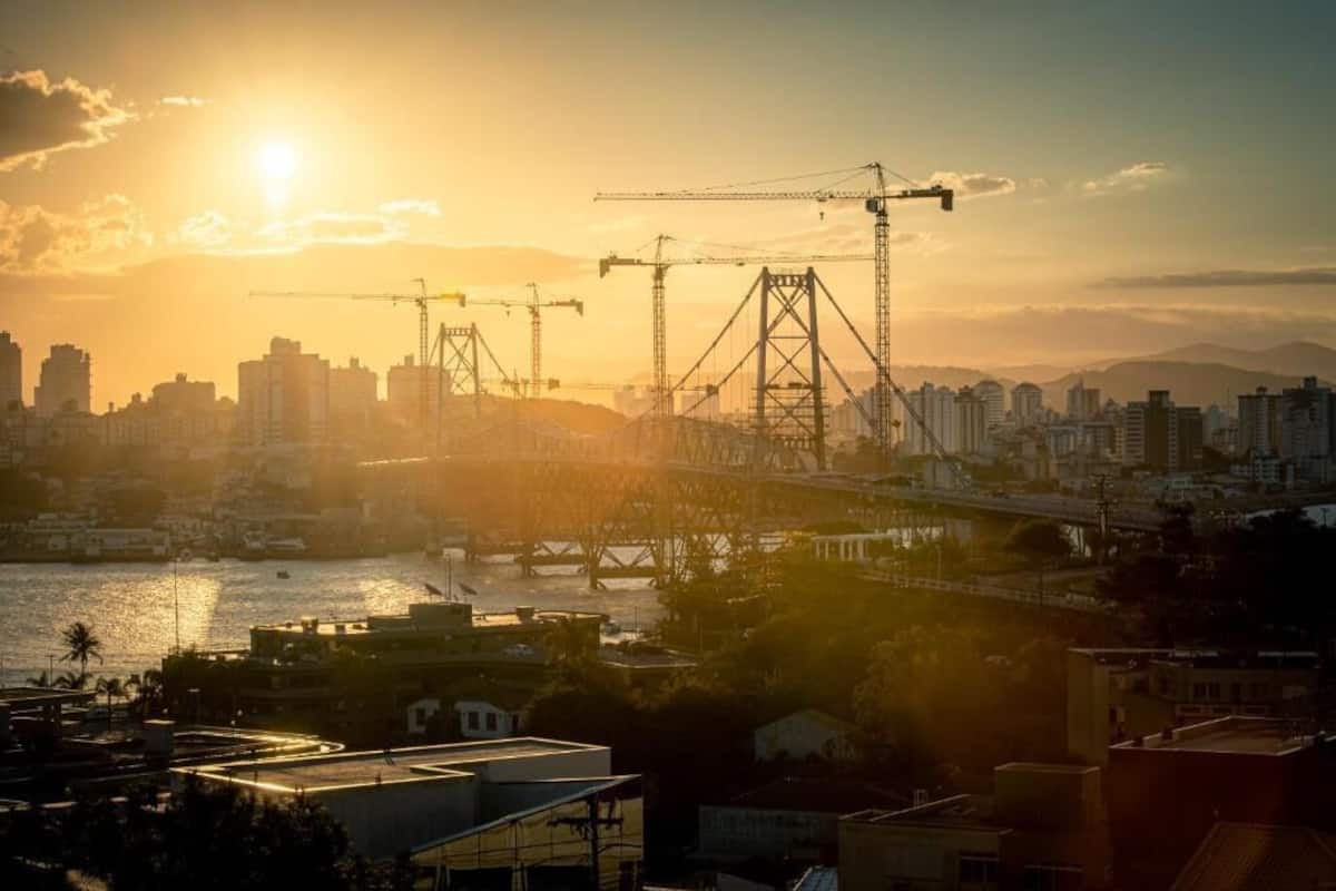 A cityscape with a bridge and construction cranes during sunset.
