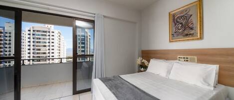 Un cuarto de hotel con una cama grande, vistas de edificios altos y una obra de arte enmarcada en la pared.