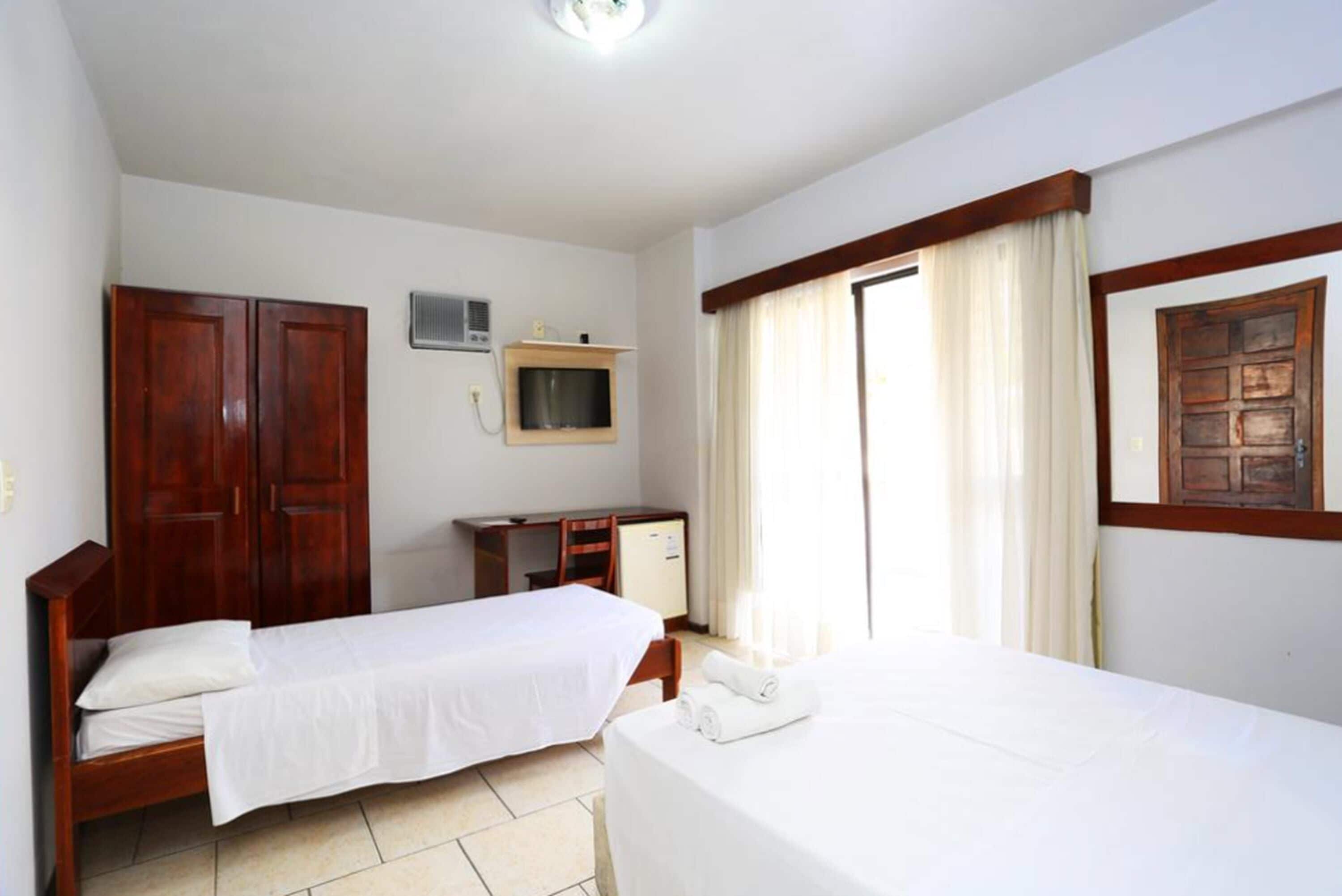 Een hotelkamer met twee éénpersoonsbedden, een bureau met stoel, een kledingkast, een televisie en een raam met gordijnen.
