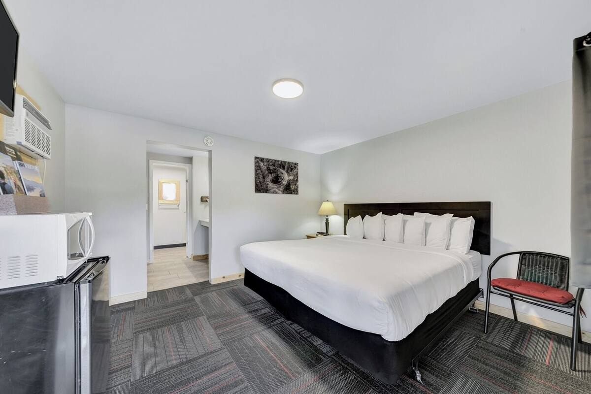 Habitación de hotel con una cama grande, un escritorio con computadora, una silla y un refrigerador pequeño.