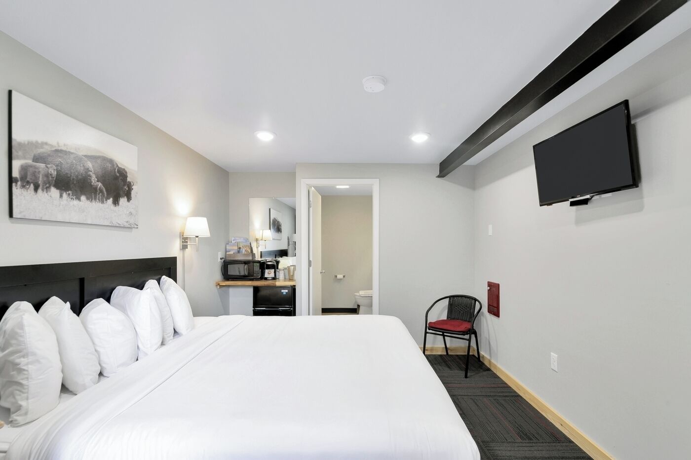 A hotel room with a large bed, a flat-screen TV mounted on the wall, a small kitchenette, and a chair.