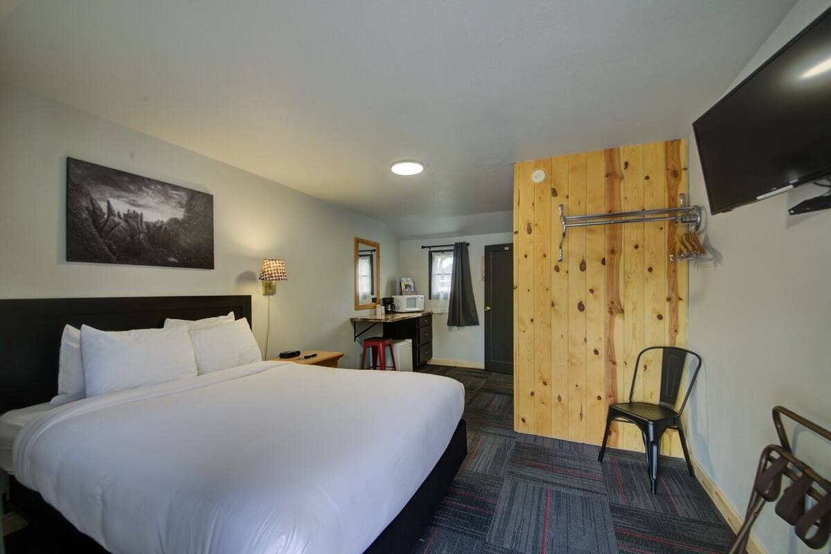 Habitación de hotel con una cama grande, un escritorio con silla, un televisor montado en la pared y un separador de madera.