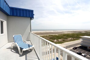 A balcony with a blue-striped lounge chair, a view of the beach, and a parking area. - Adventurer Oceanfront Inn (Wildwood Crest)