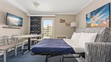 A hotel room with a bed, a desk, a chair, a TV, and a painting of a carnival.