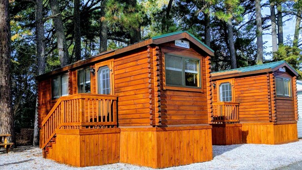 Two log cabins with wooden decks and windows, surrounded by trees. - Anvil Campground (Williamsburg)