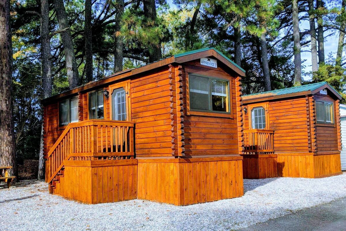 Two log cabins with wooden decks and windows, surrounded by trees.