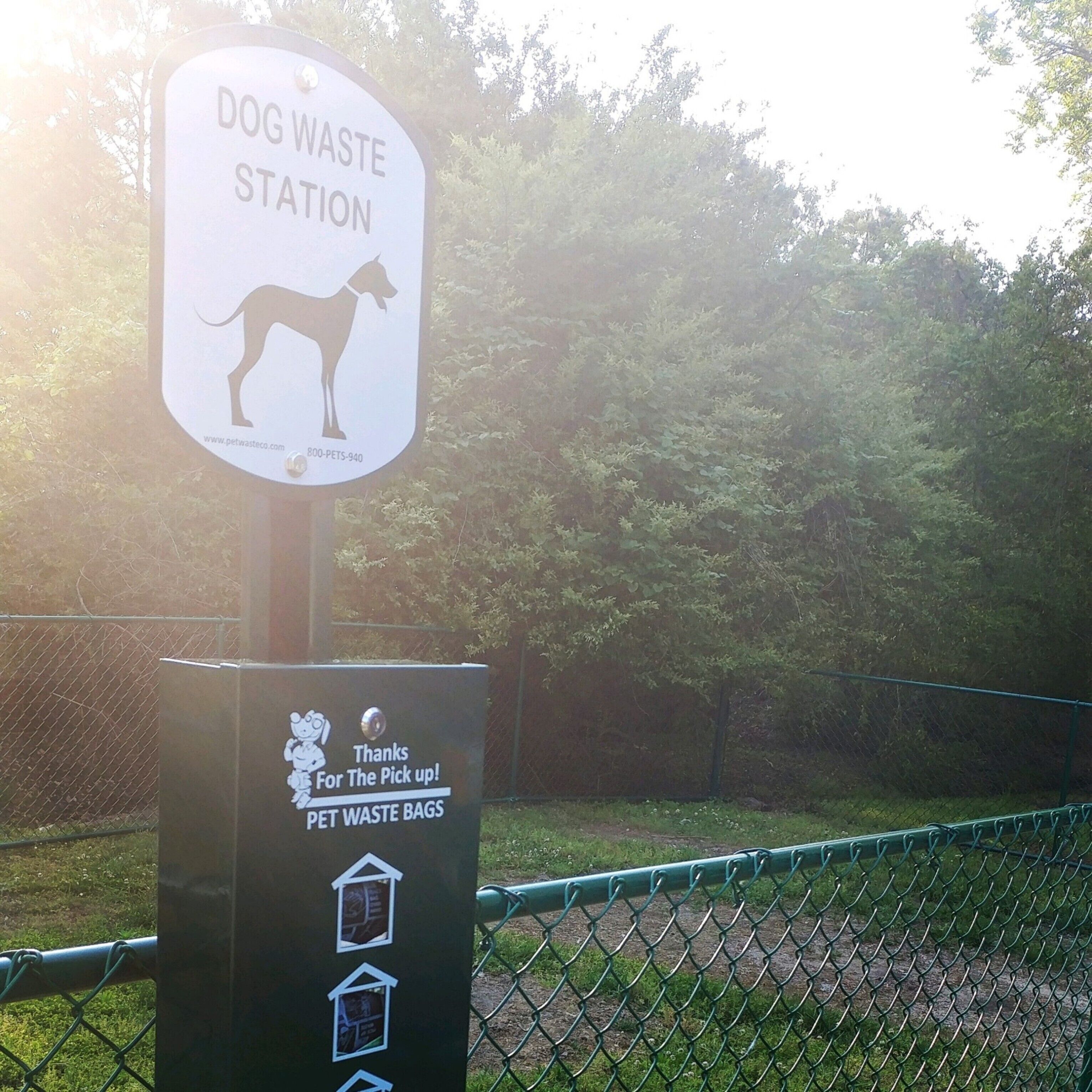 A dog waste station with a sign and a trash bin.