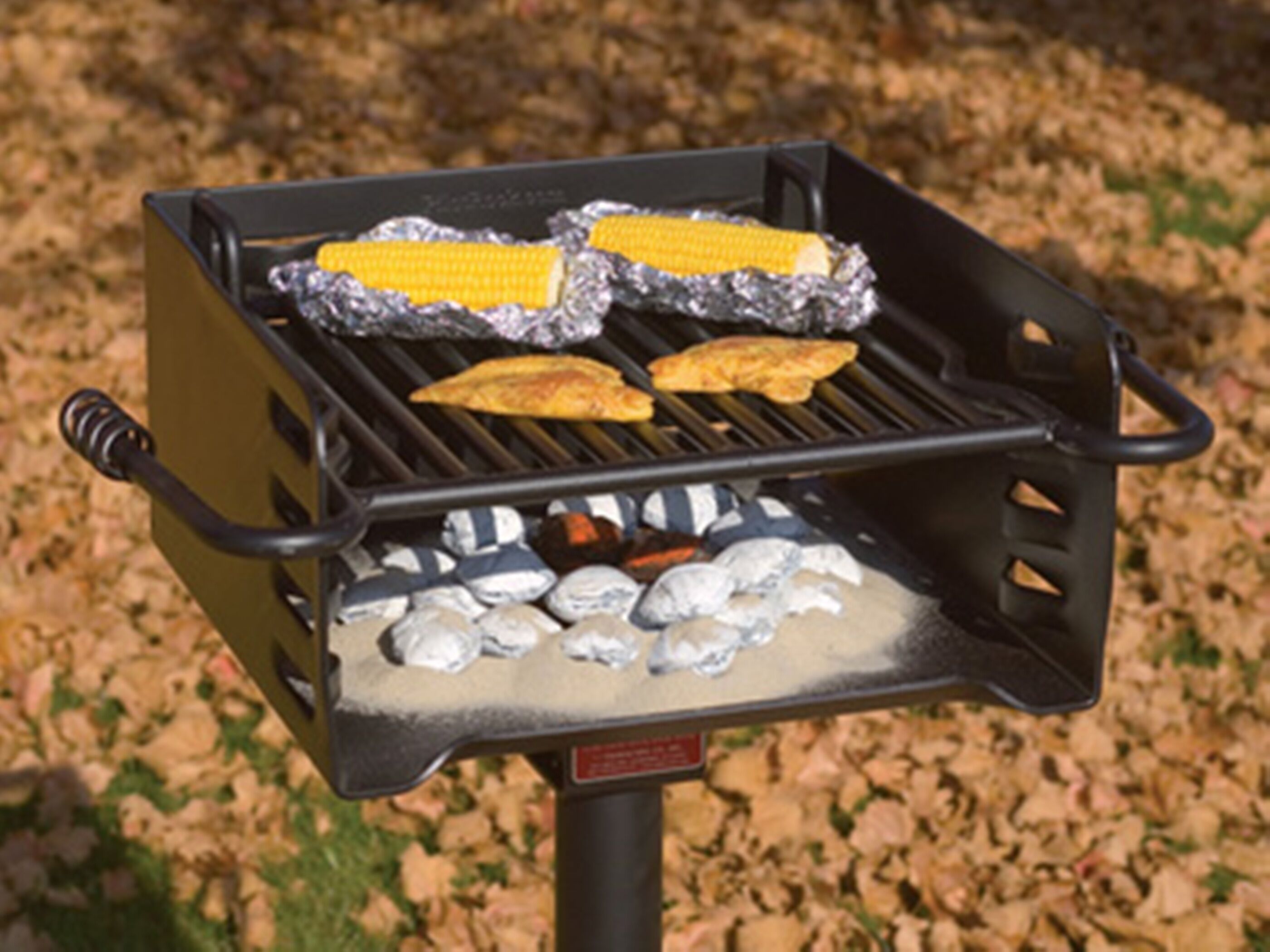 Ein Grill mit Lebensmittel in Alufolie, darunter Mais und Hähnchen, auf einem Rost.