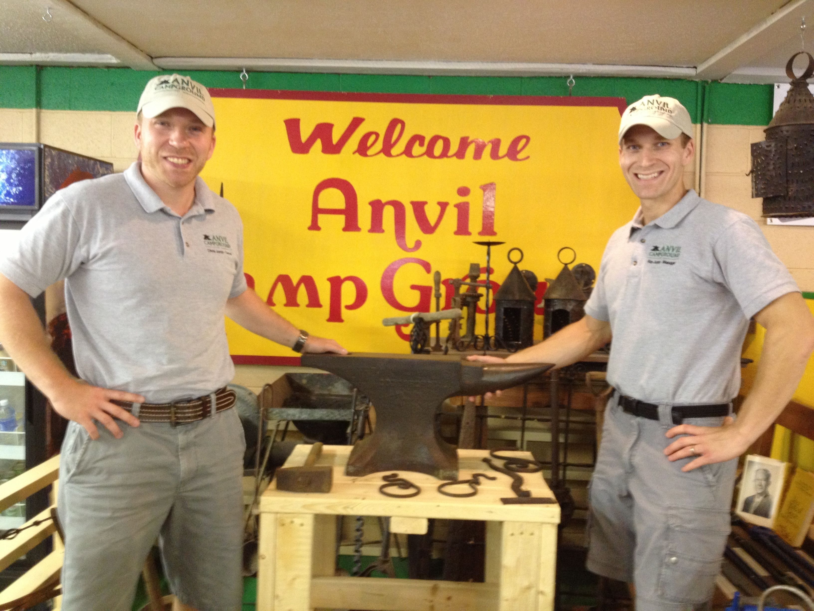 Deux hommes se trouvent dans un atelier, et on peut voir en arrière-plan une pancarte indiquant « Bienvenue au camping Anvil ».