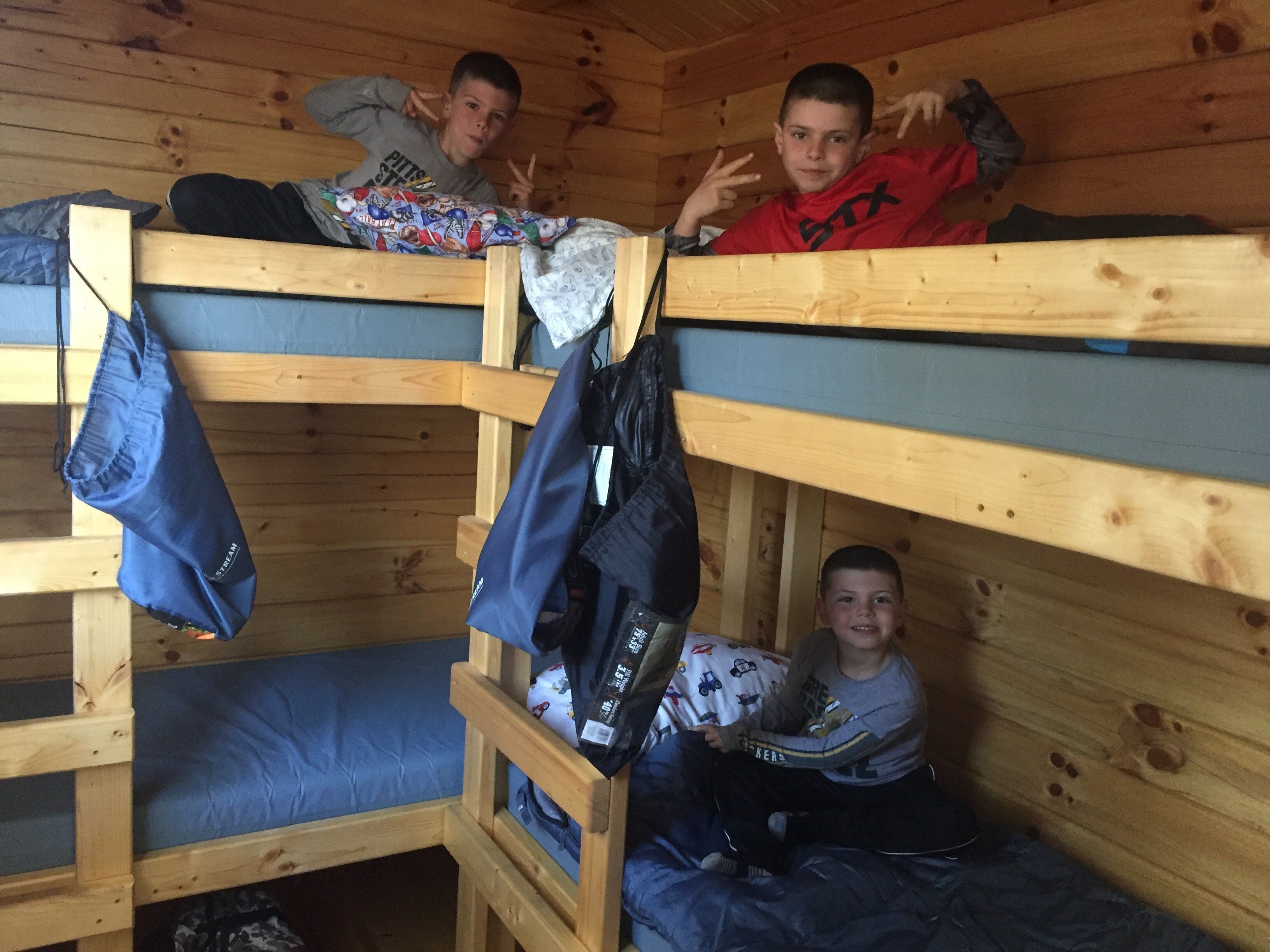 A bunk bed room with three wooden bunk beds, each with a blue mattress. There are clothes hanging on the side of the beds.