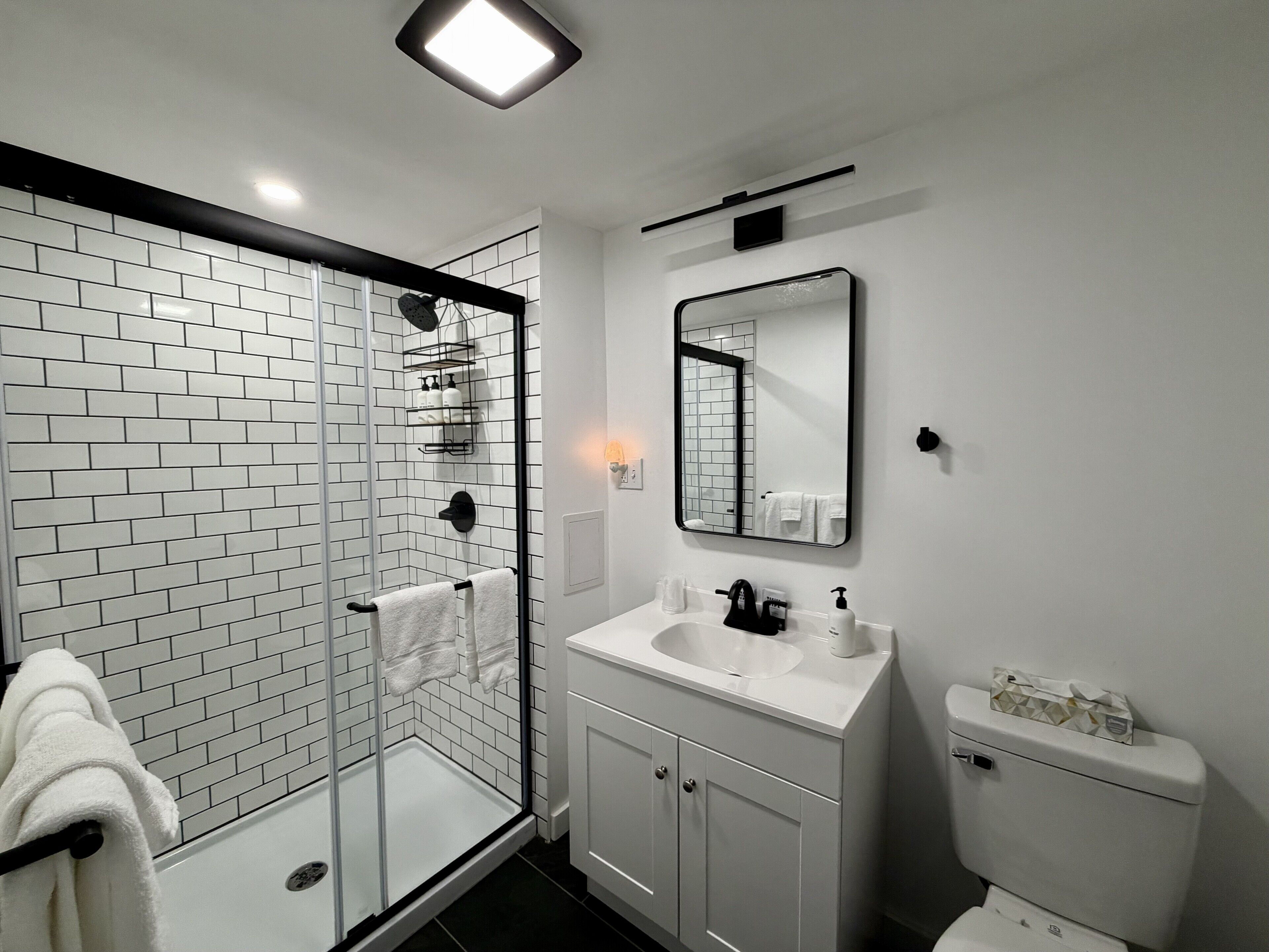 A modern bathroom with a glass shower enclosure, white tiled walls, a white sink, and a toilet.