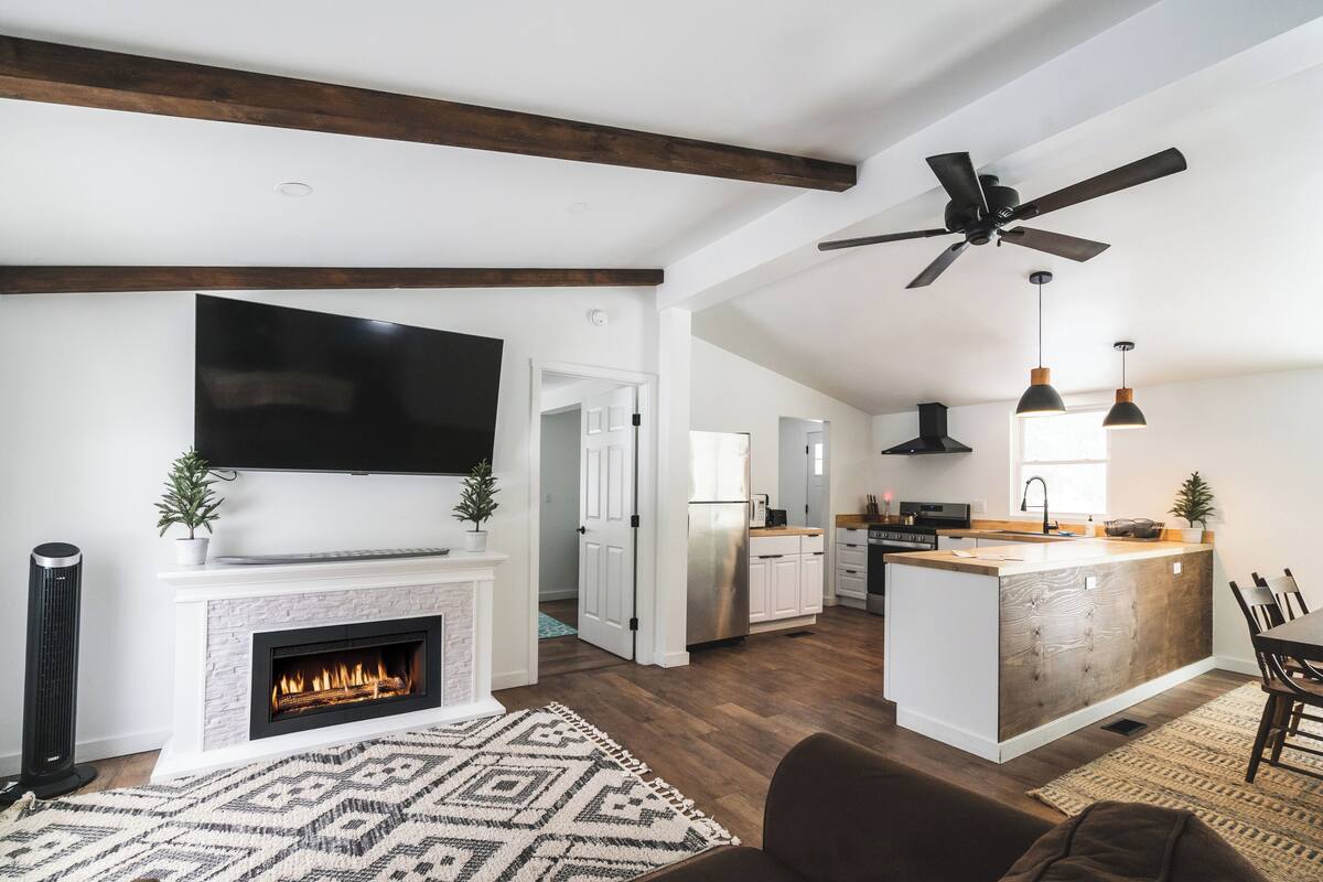 A modern kitchen with a central island, a fireplace, and a dining area with a brown sofa.