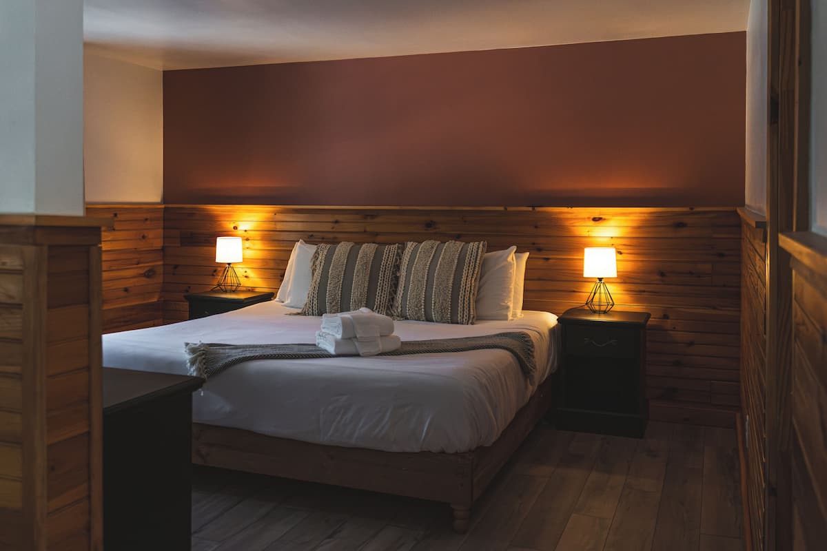 A neatly made bed with pillows and a blanket, two bedside lamps, and wooden paneling on the walls.