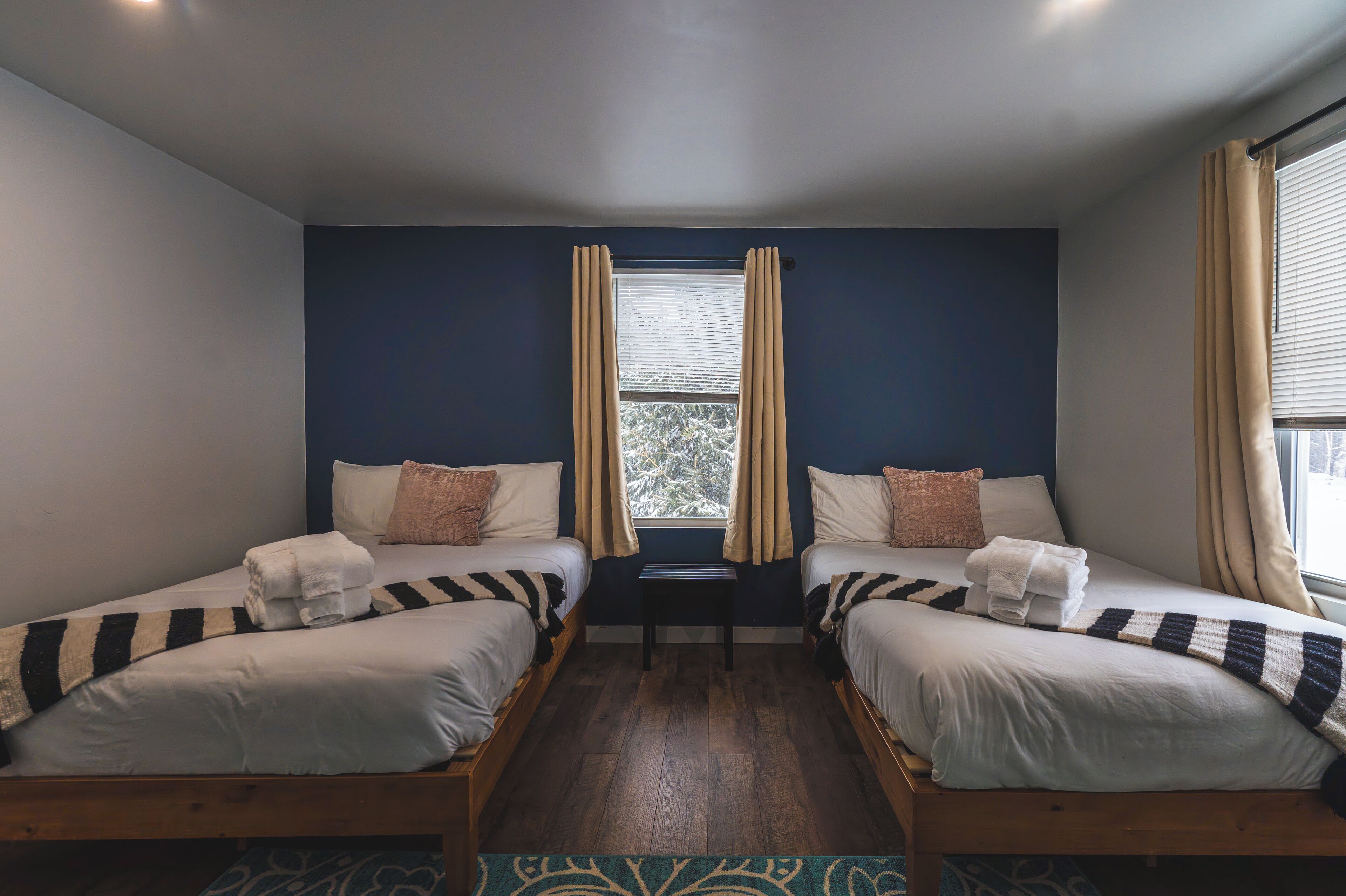 A room with two single beds, a small table, and a window with curtains.