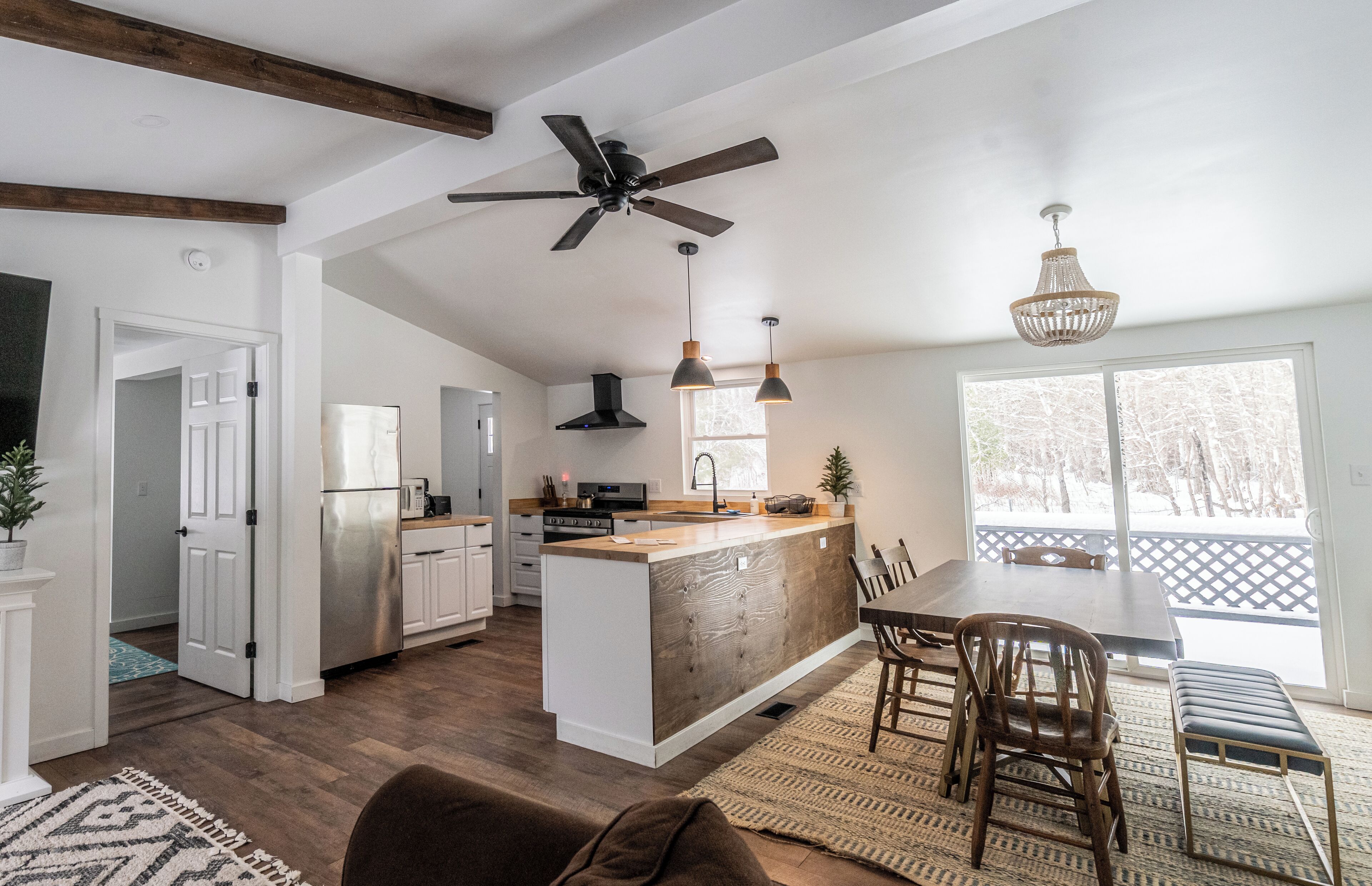 Une cuisine moderne dotée d’un îlot central, de poutres en bois au plafond et de luminaires suspendus.