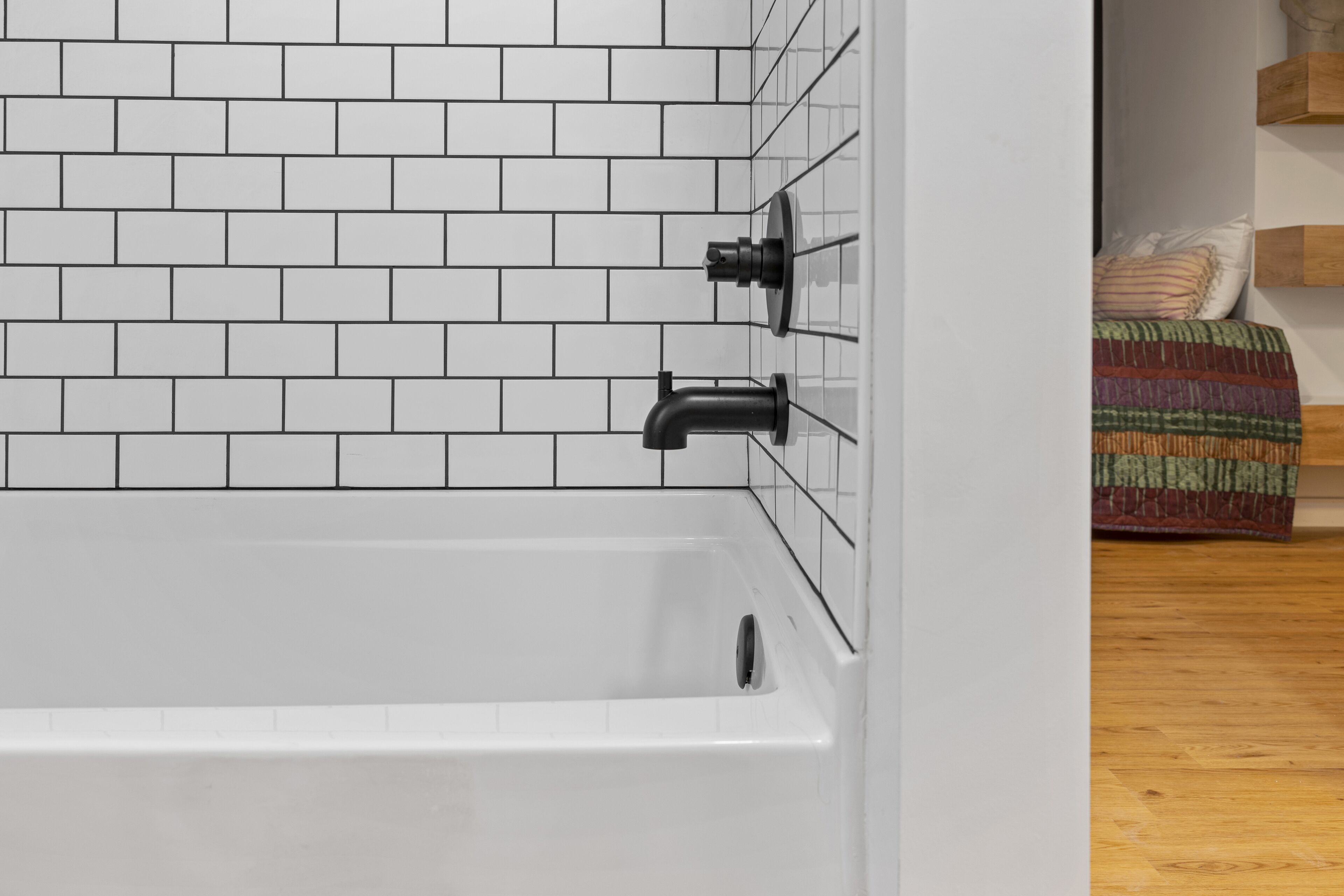 A bathroom with white tiled walls and a white bathtub.