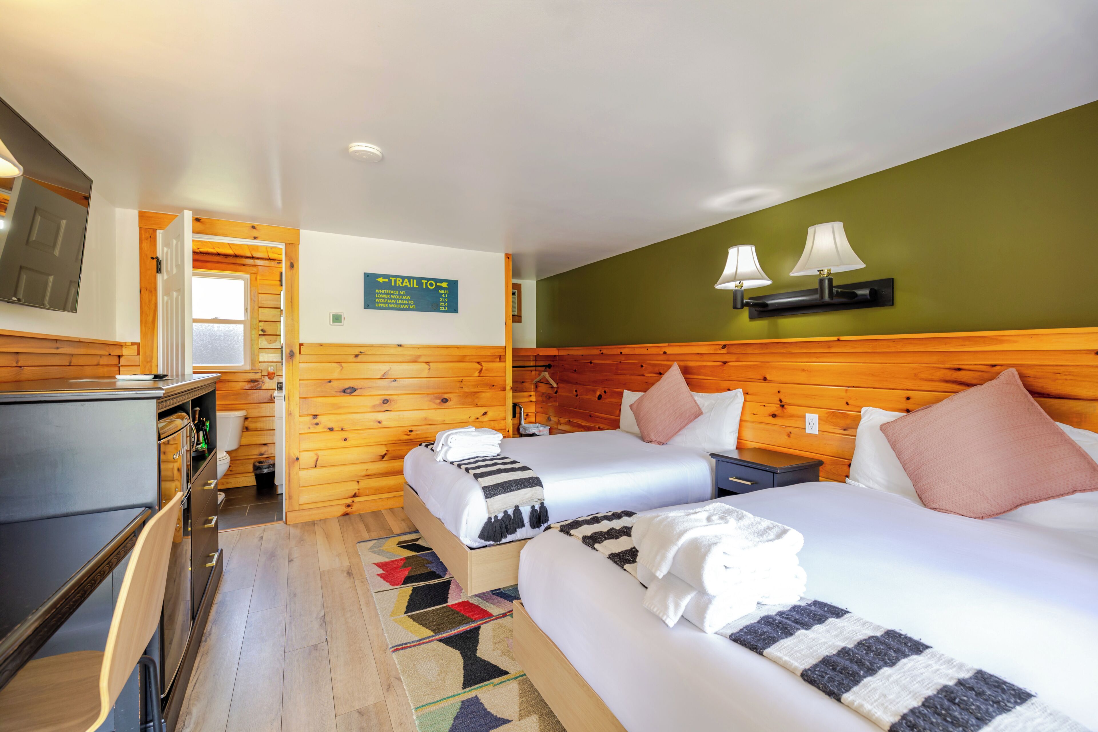 Habitación de hotel con dos camas, un escritorio, una silla y una pequeña kitchenette.