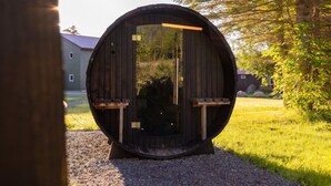 Eine große Hollfasskonstruktion mit Glastür, zwei Holzsitzen und einem Kiesweg, der davor führt.