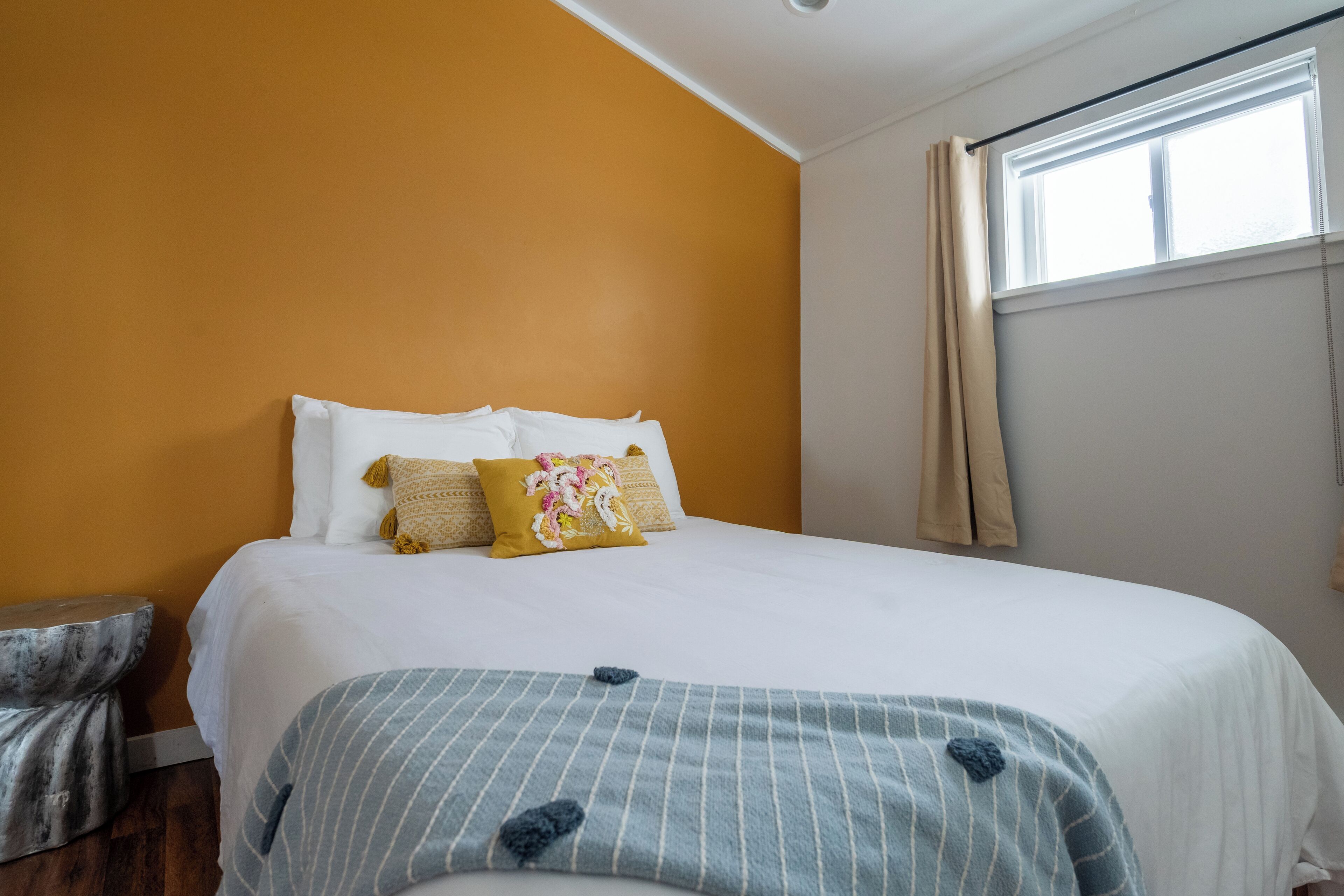 A bedroom with a bed, a window with curtains, and a nightstand.