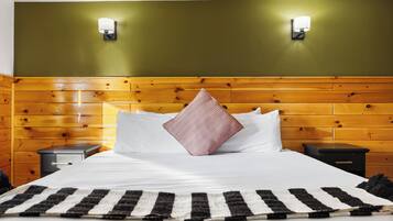 A hotel room with a wooden headboard, two bedside tables, a bed with white bedding, a striped rug, and two wall-mounted light fixtures.