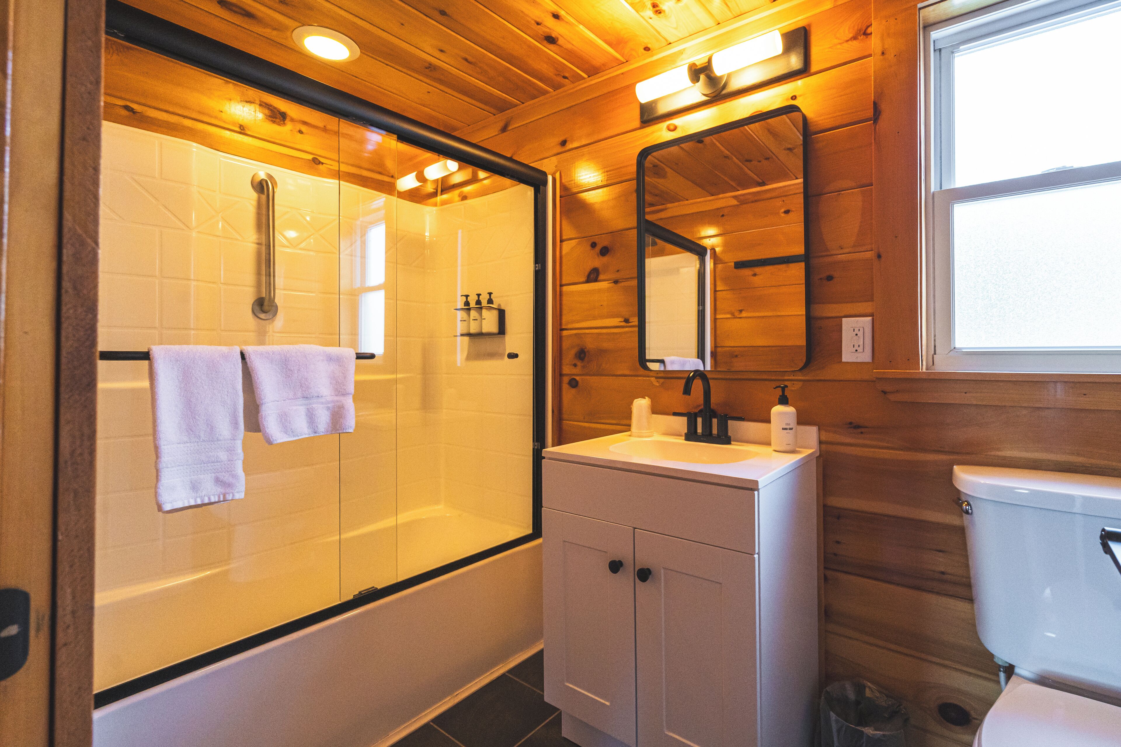 A wooden cabin bathroom with a glass-enclosed shower, a sink, and a toilet.