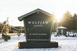 Una cabaña de madera llamada 'Wolfjaw Lodge' con un letrero que indica que es de 'White Rainbow'.