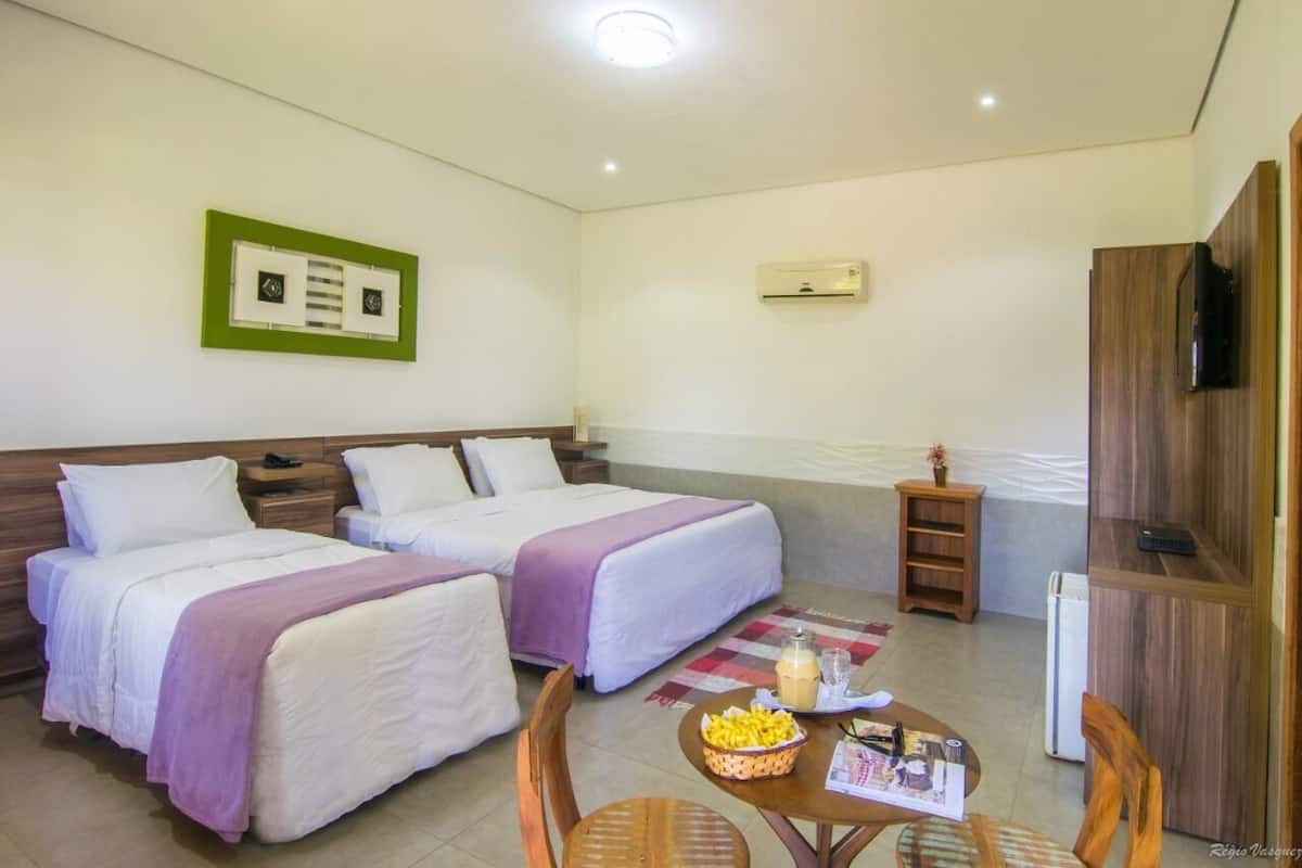 A hotel room with two beds, a small table with snacks, a TV, and a wooden cabinet.