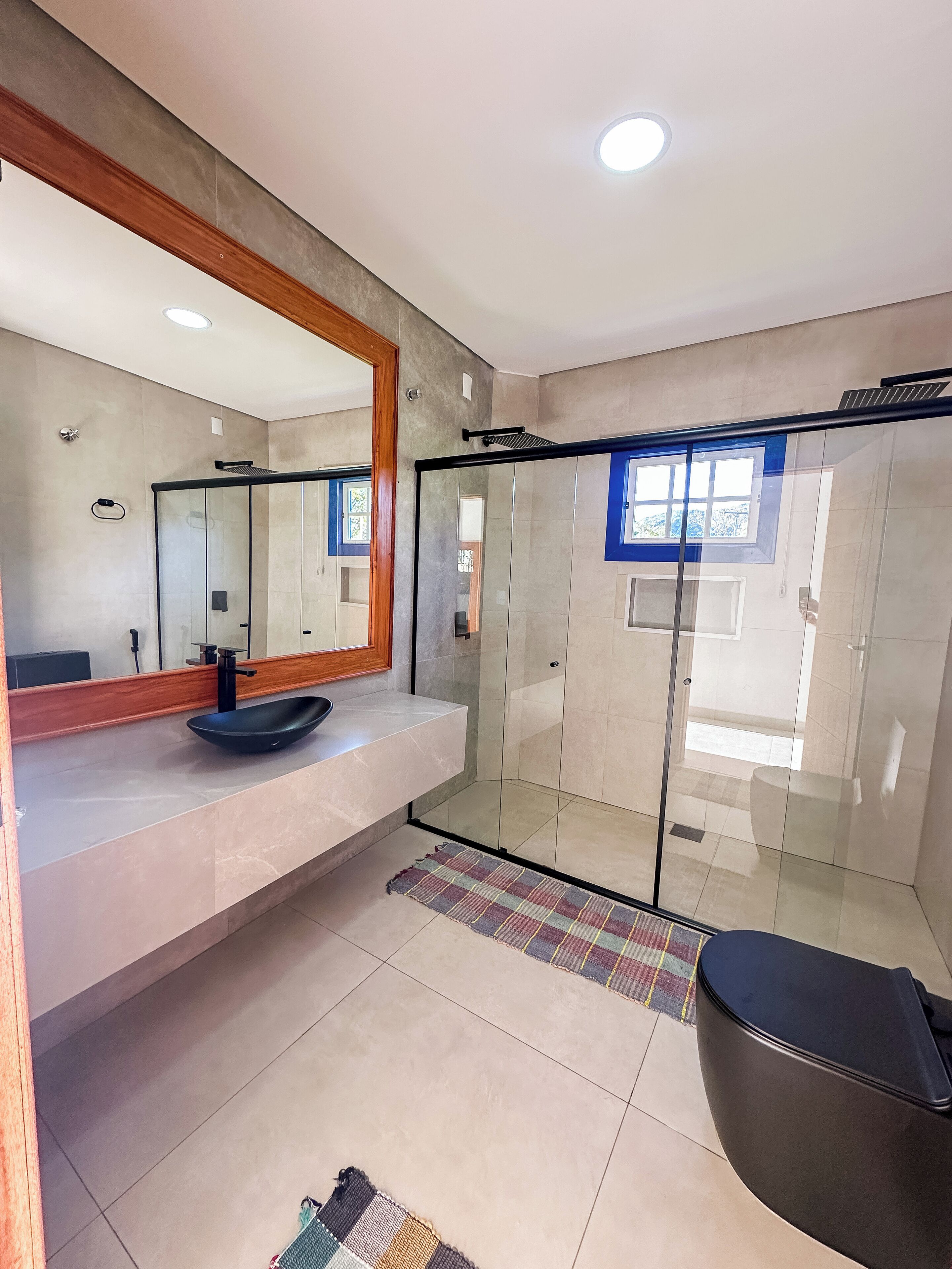 A modern bathroom with a glass shower enclosure, a large mirror, and a black bathtub.