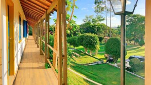 A covered walkway with wooden flooring and a view of a landscaped garden with trees and a car. - Hotel Pontal de Tiradentes (Tiradentes)