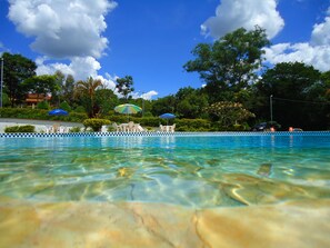 Una piscina cristalina con sillas de descanso y sombrillas, rodeada de exuberante follaje y árboles.