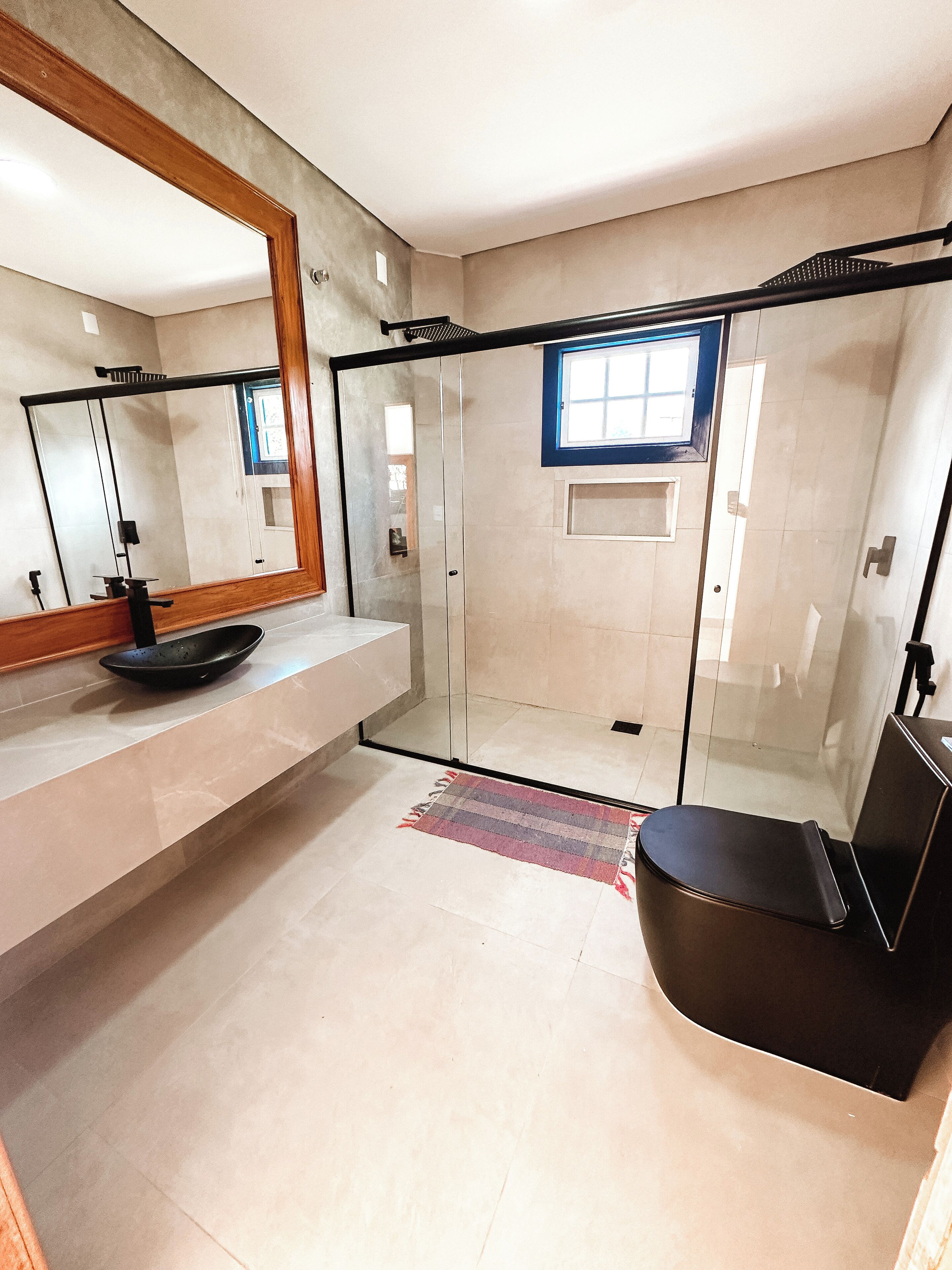 A modern bathroom with a glass shower enclosure, a large mirror, and a black chair.