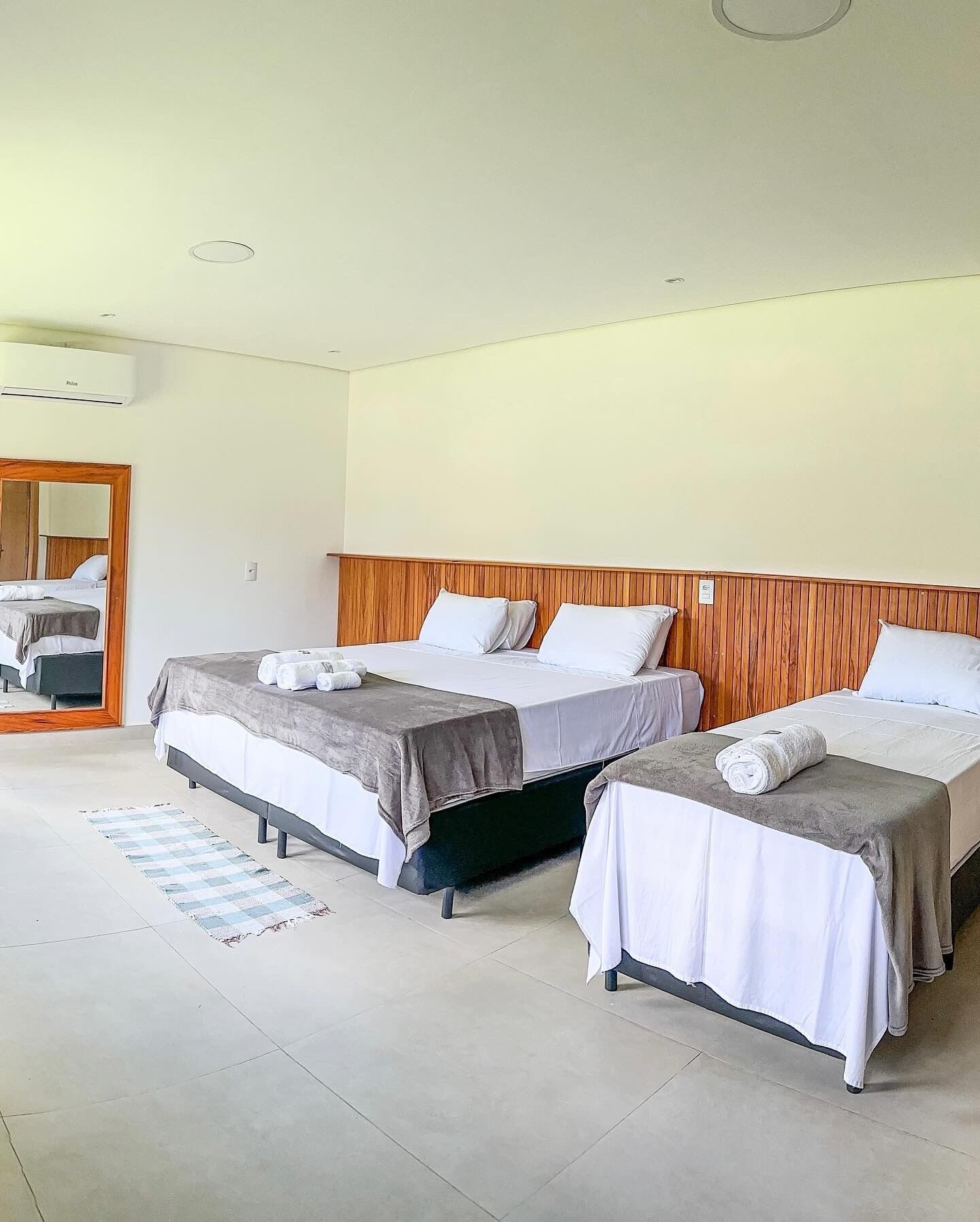 Une chambre d’hôtel avec deux lits, une tête de lit en bois, un grand miroir et un sol carrelé.