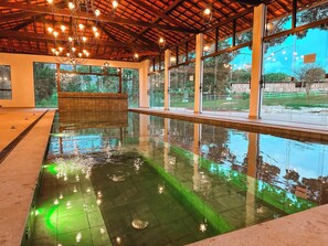 An indoor swimming pool with clear water, a tiled floor, and a wooden ceiling with hanging lights. - Hotel Pontal de Tiradentes (Tiradentes)