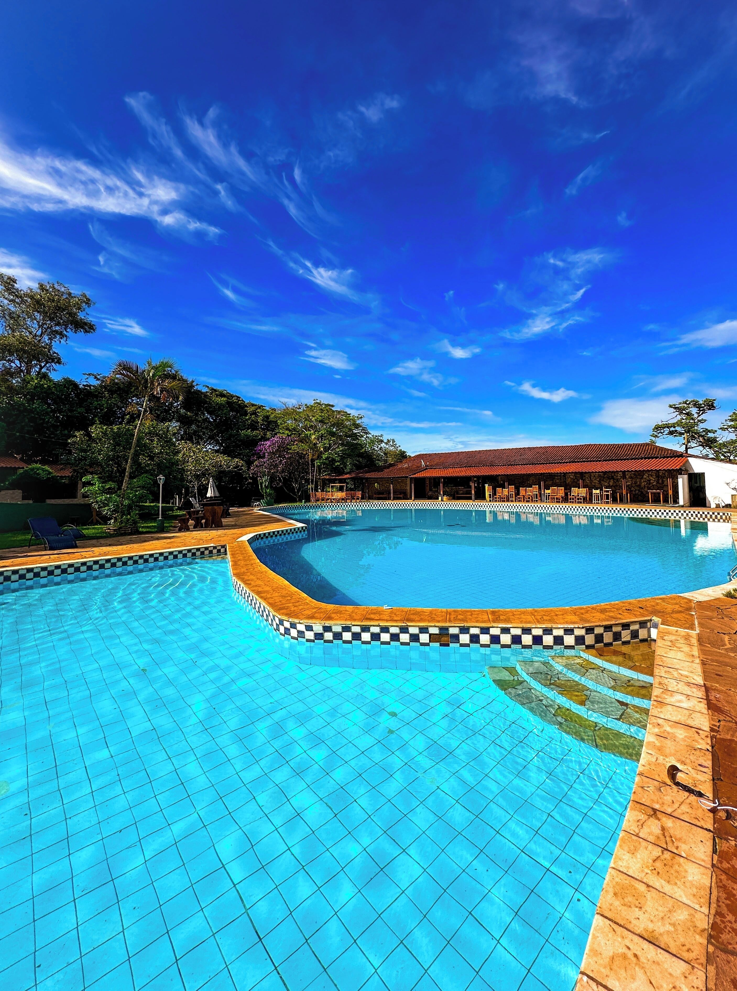 A large outdoor swimming pool with a tiled edge, surrounded by a covered seating area and trees.