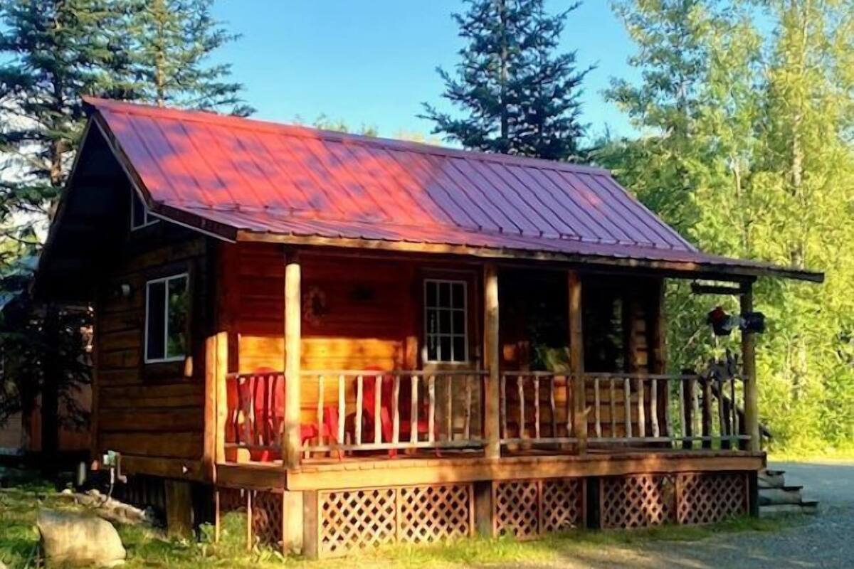 A rustic cabin with a red metal roof, a wooden porch, and a lattice fence.