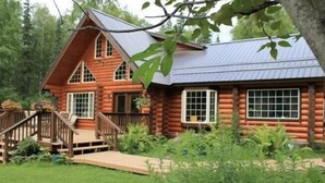Une cabane en rondins avec un escalier en bois, une véranda et un toit en métal.